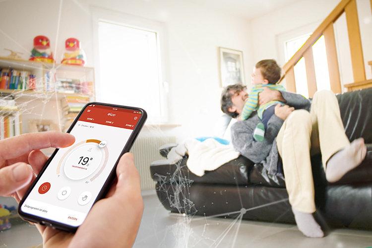 Una persona tiene in mano uno smartphone con l'app Remocon Net aperta. Sullo sfondo, un padre gioca con suo figlio.